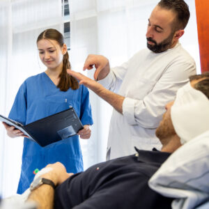 Arzt erklärt Patientin während der Visite Befunde, unterstützt von Assistenzärztin.