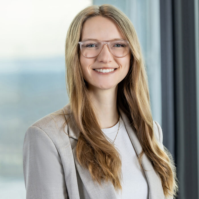 Junge Frau im Businessoutfit lächelt in modernem Bürogebäude – professionelles Businessportrait