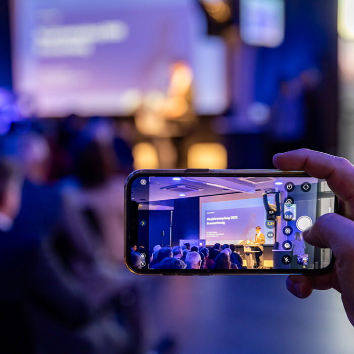 Neujahrsempfang der Deutschen Bank in Braunschweig mit Gästen aus Frankfurt. Ein Mensch hält das Handy hoch um die die Bühne zu fotografieren